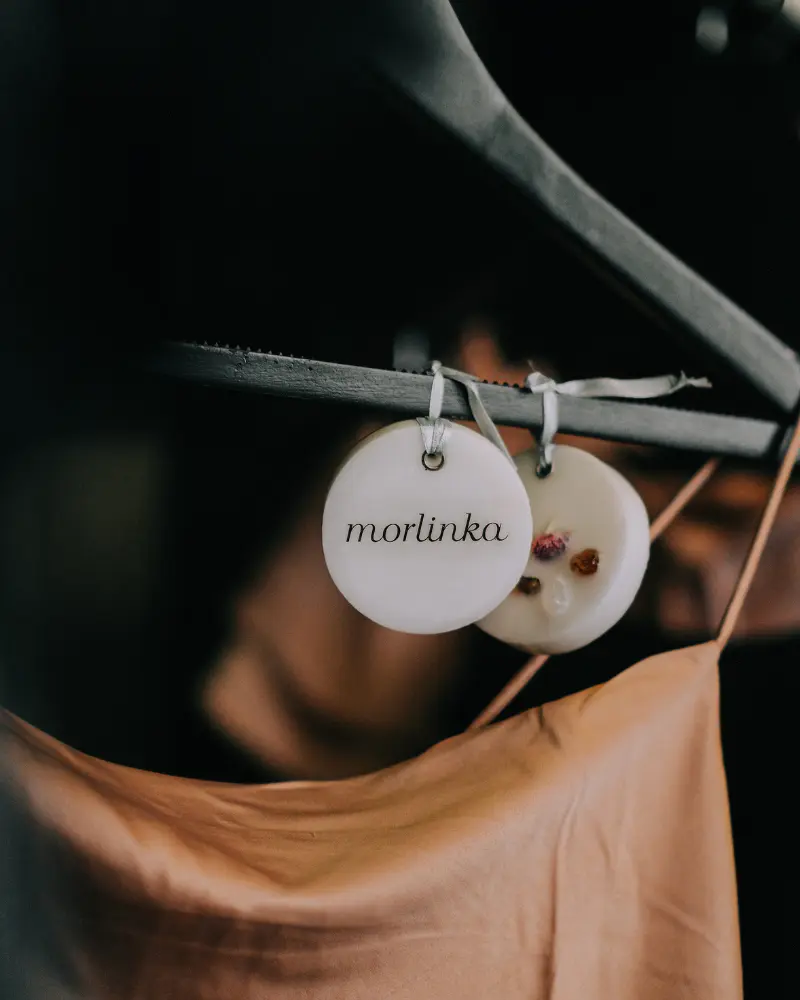 Two Morlinka scented wax tablets hanging from a wooden hanger against a soft fabric background, showcasing elegant and minimal branding.