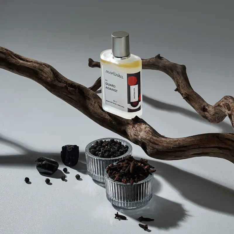 Morlinka “Guard Against” crystal mist displayed on a gray surface with natural wood and spices, reflecting protective and grounding energy.