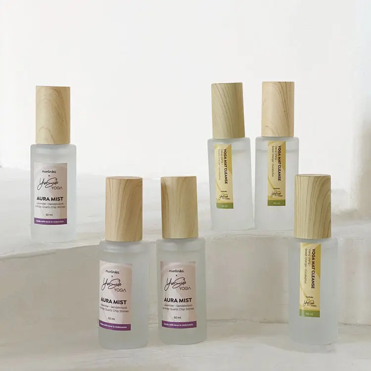 A collection of Morlinka x Yinside Yoga aura mists displayed on white steps, featuring frosted glass bottles with wooden caps and minimalist labels in purple and green tones.